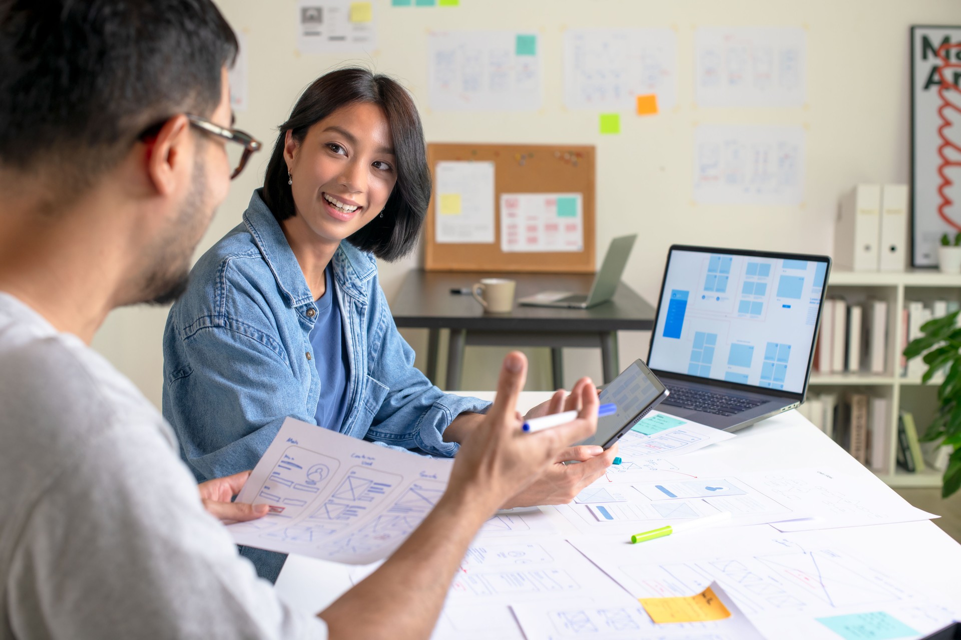 UX/UI designers discussing and brainstorming on wireframes for a website and mobile app prototype, surrounded by sketches of user flow and design tools, in the concept of website and mobile application design concept.